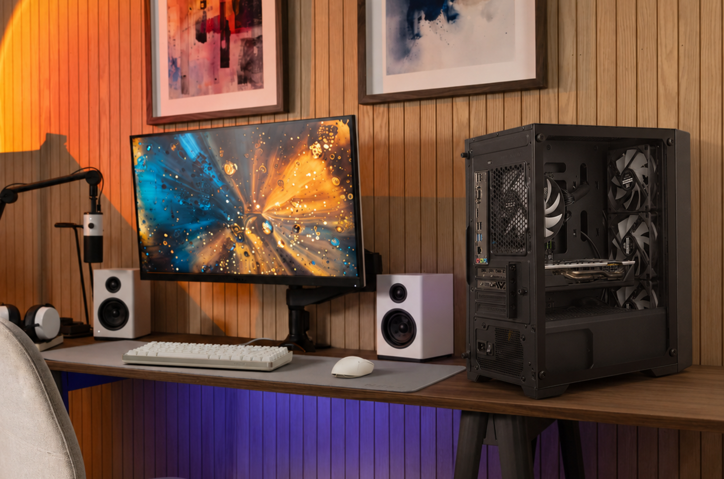 Black mesh-front gaming PC on a wood desk beside a monitor and speakers