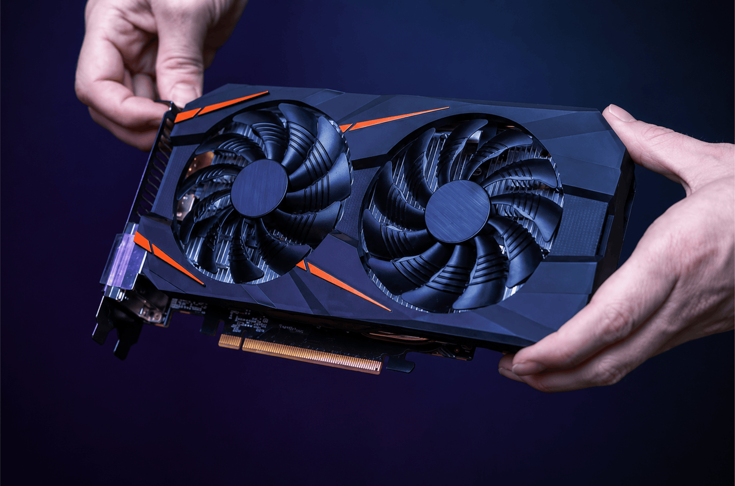 Hands holding a black dual-fan graphics card against a dark background